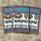Three printed promotional cards or flyers for tribal tattoo designs are arranged overlapping on a textured beige fabric surface. The cards feature the text 'Official Tattoo Brand Tribal Tattoos' and display black tribal line art, floral motifs, a sugar skull, and blue wave designs.